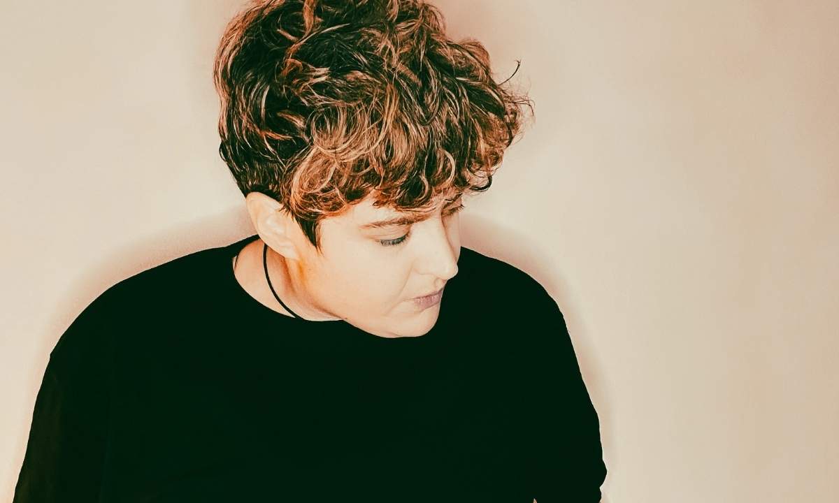 Ritratto della cantautrice Annarè con lo sguardo rivolto verso il basso, su sfondo dalle tonalità calde.