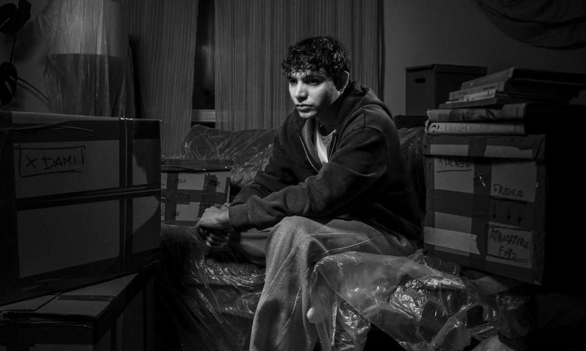 eroCaddeo seduto tra scatoloni da trasloco in una foto in bianco e nero per il singolo lontano da casa