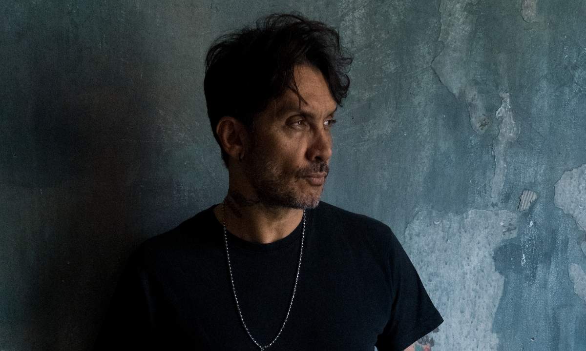 Fabrizio Moro, ospite di Da noi a ruota libera, in posa di profilo su sfondo grigio scrostato, foto promozionale 2026