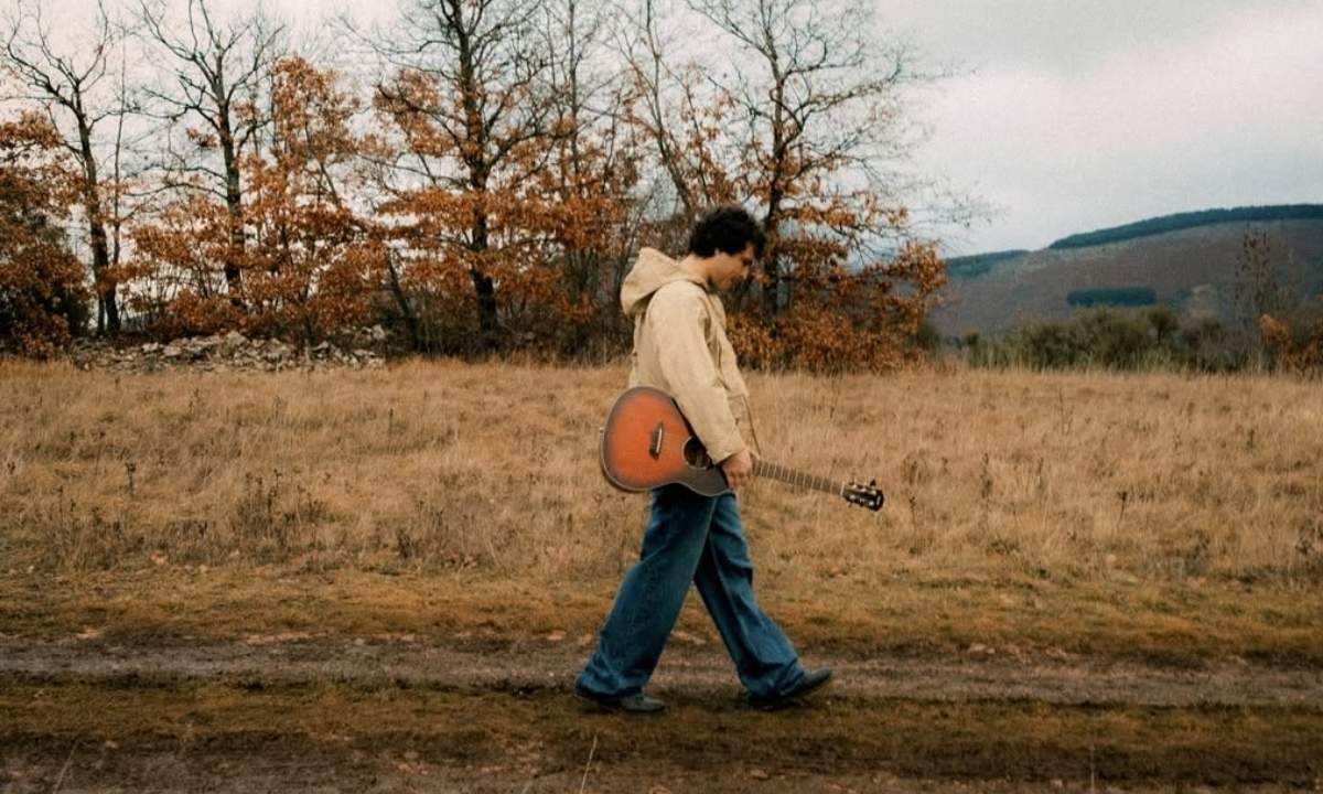 Leo Gassmann cammina in un prato con una chitarra in spalla nell’immagine usata per l’articolo su Girasole