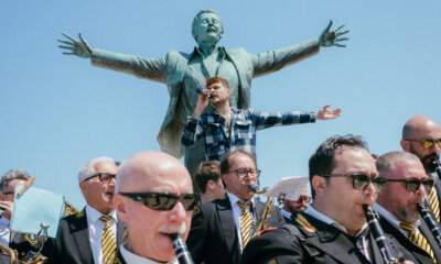 Renzo Rubino canta davanti alla statua di Domenico Modugno a Polignano a Mare con la banda musicale durante la rassegna Città della Musica 2026