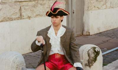 Primogenito seduto su un marciapiede con cappello a tricorno, giacca a quadri e pantaloncini da boxe rossi