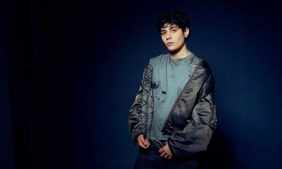 Senza Cri posa su sfondo blu scuro indossando una t-shirt strappata e un bomber aperto (Foto: Bex Gunther)