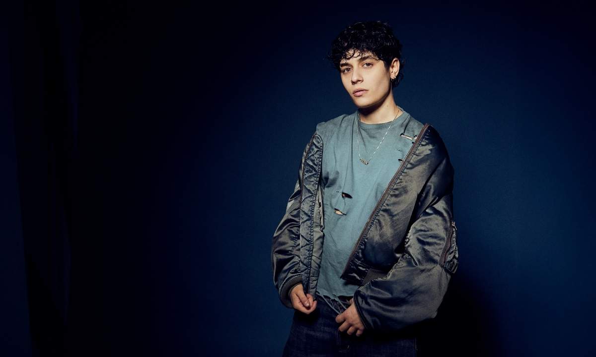 Senza Cri posa su sfondo blu scuro indossando una t-shirt strappata e un bomber aperto (Foto: Bex Gunther)