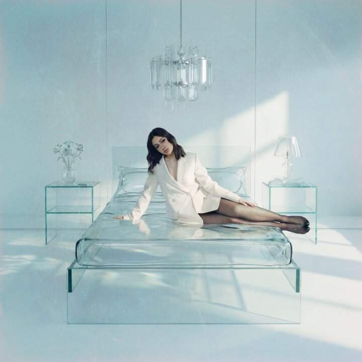 Copertina dell'EP Sogni di Vetro di Angie: la cantante in giacca bianca seduta su un letto trasparente in una stanza di vetro
