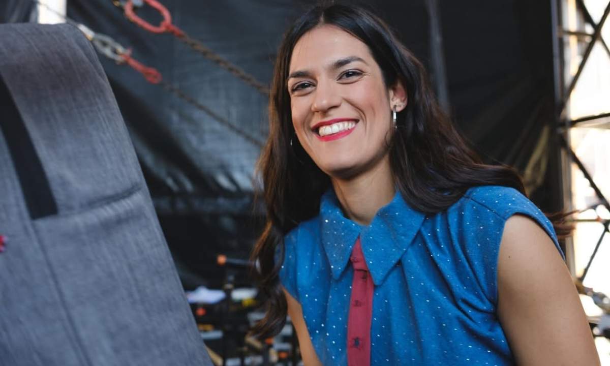 Bambina sorride dietro le quinte del palco di 1MNEXT 2026, indossa una blusa blu a pois bianchi e cravattino bordeaux
