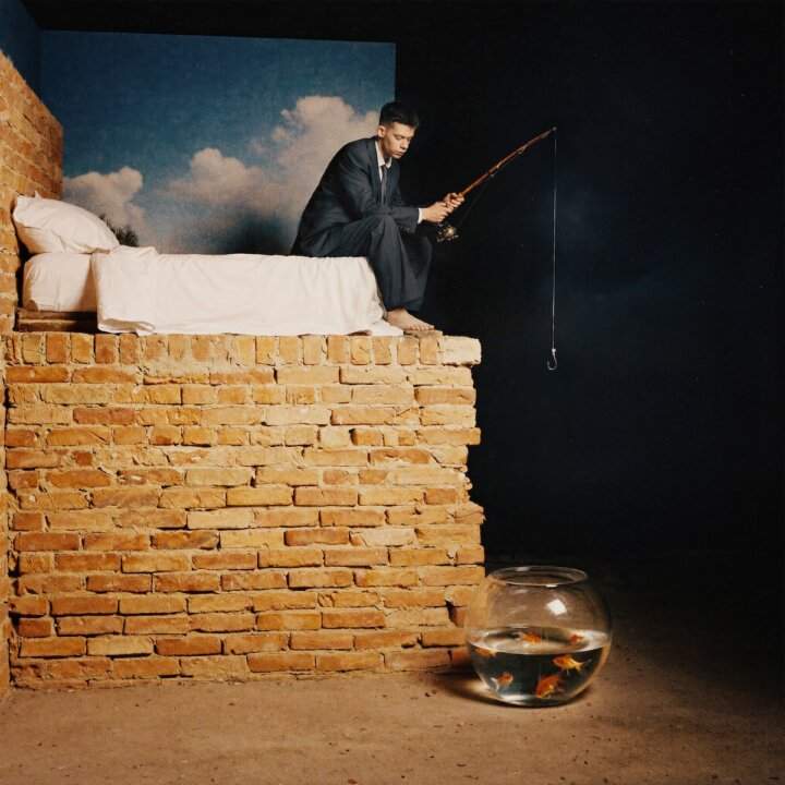 Cover dell'album Fase REM di Leon Faun: il rapper sul letto pesca con l'amo verso un acquario sul pavimento.
