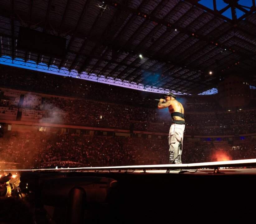 Geolier sings into the microphone on the San Siro stage under the lights of the show
