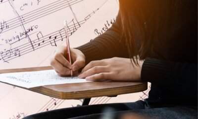 Studente compila la scheda di una prova d'esame su sfondo di spartiti musicali. Maturità 2026, partitura errata al liceo musicale