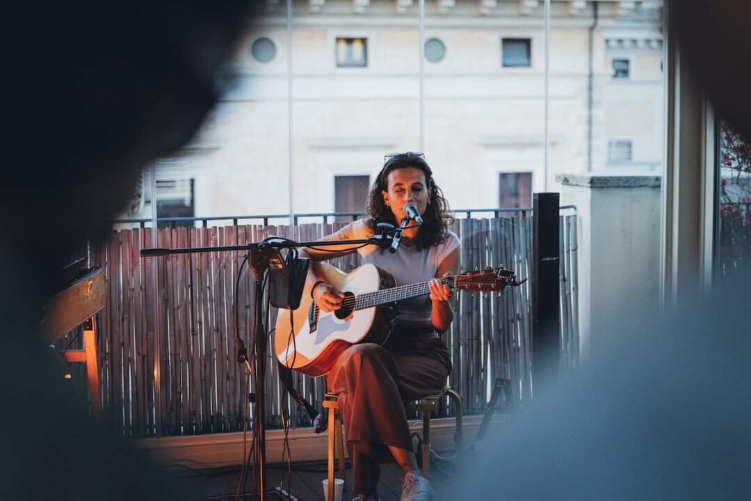 Two musicians, violin and acoustic guitar, during a Music Suite live performance on the terrace overlooking the buildings of Rome