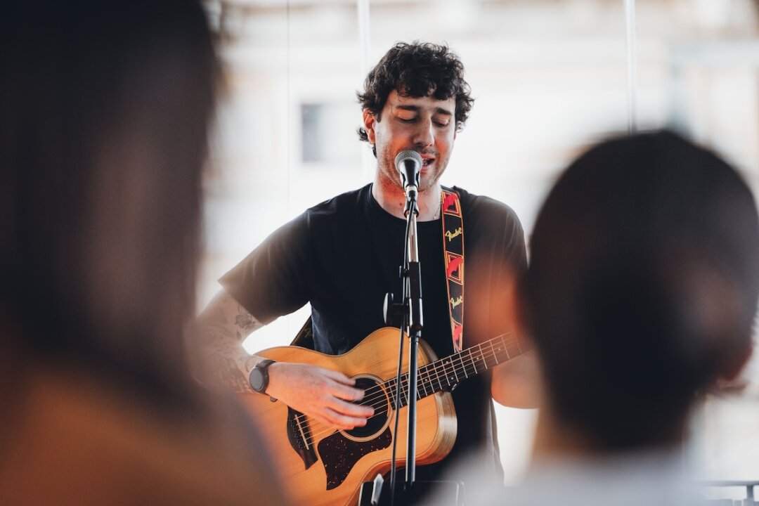 A singer-songwriter with an acoustic guitar sings in front of a close audience during a Music Suite live show in Rome