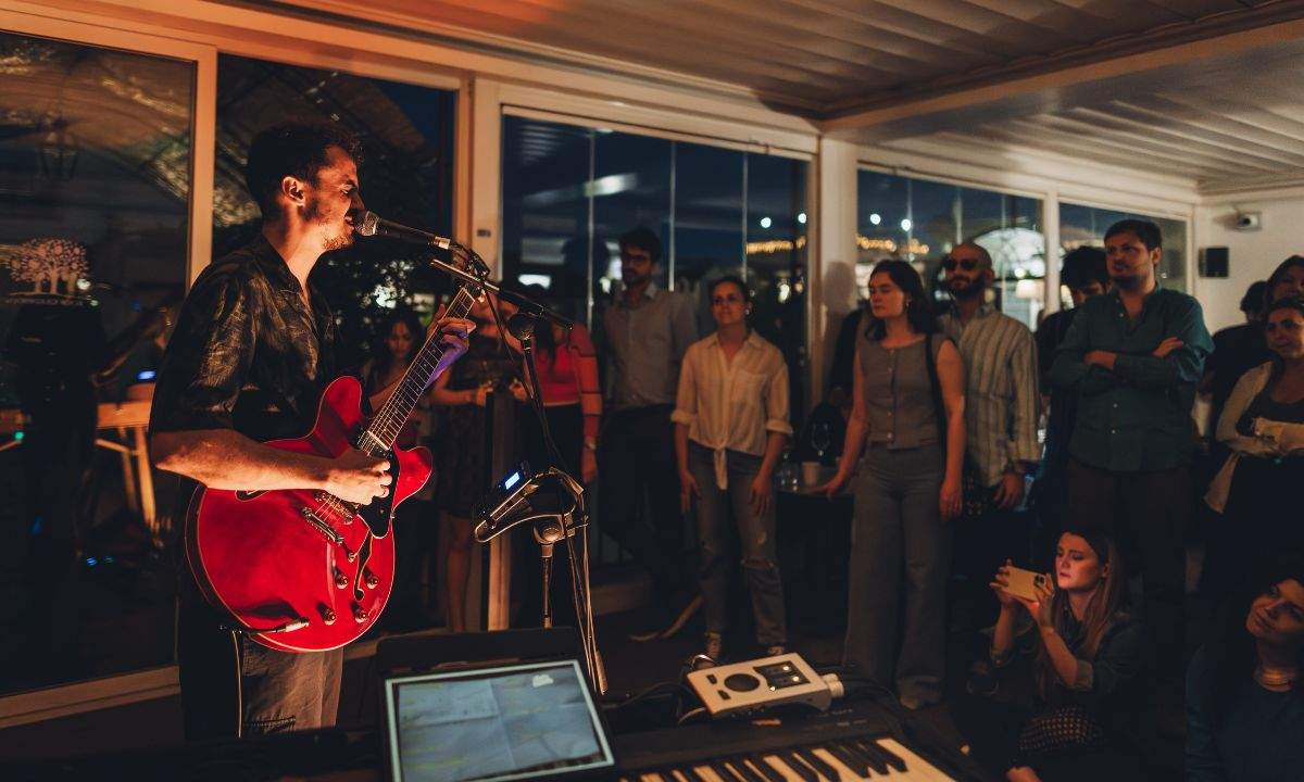 Concerto Music Suite sul rooftop dell'Hotel Nord Nuova Roma: un cantautore con chitarra elettrica davanti al pubblico. Folcast