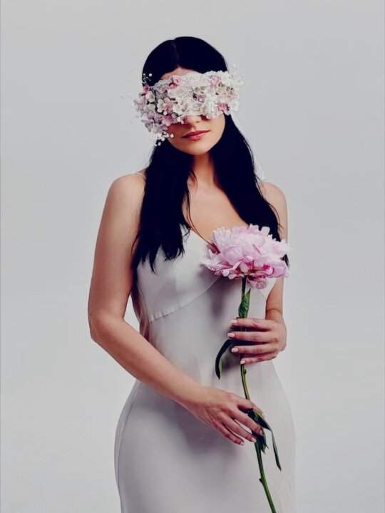 Laura Pausini with a band of white and pink flowers over her eyes and a peony in her hand, from the post with the date 7.8.2026