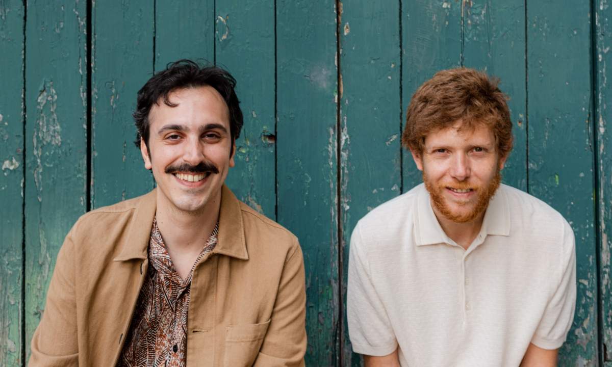 Massimo Di Lena e Lucio Aquilina dei Nu Genea sorridono davanti a una porta di legno verde