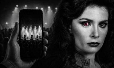 Una mano riprende un concerto con lo smartphone accanto al volto di un'aliena dei Visitors con l'occhio fucsia