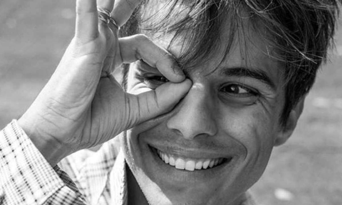 Michele Merlo sorride in un ritratto in bianco e nero, la mano davanti a un occhio