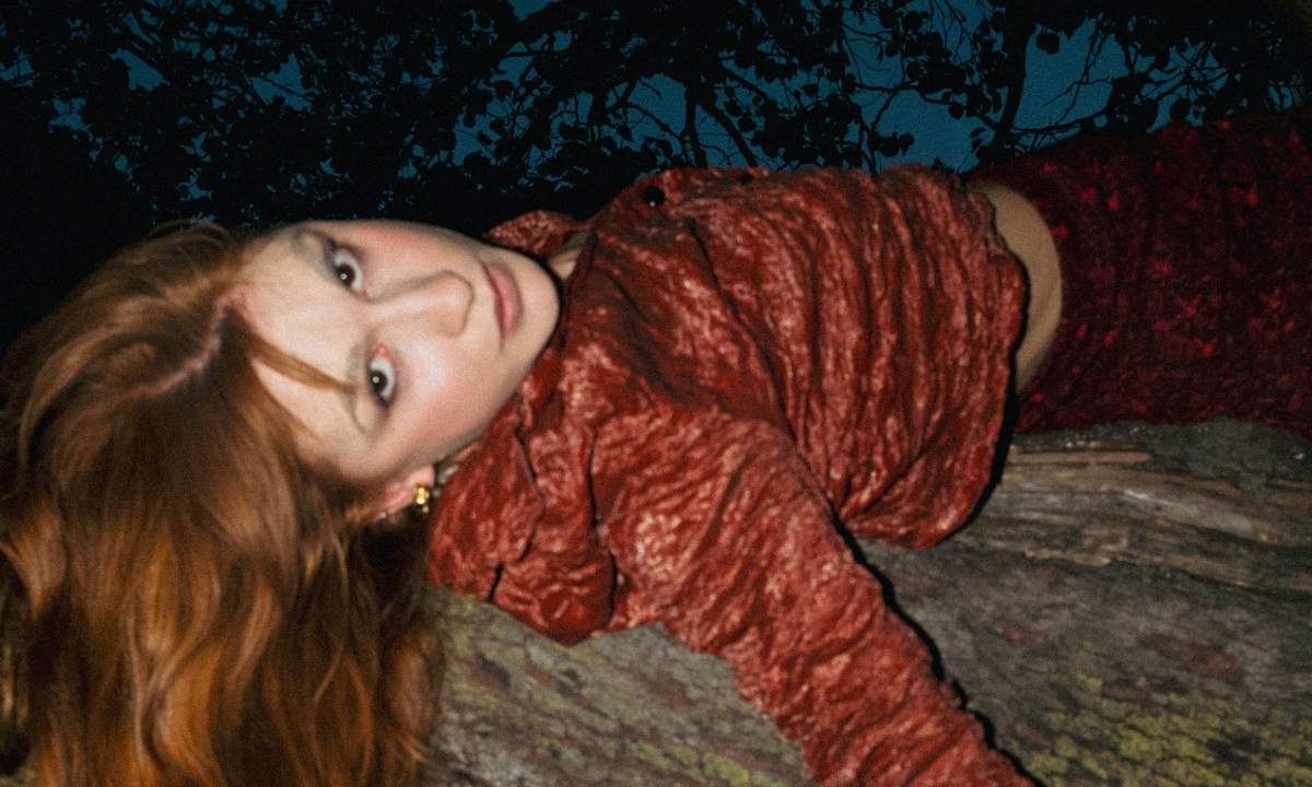 OTTOBRE distesa su un tronco con abito rosso in un bosco notturno, foto per il singolo di me che resta? con Affanno
