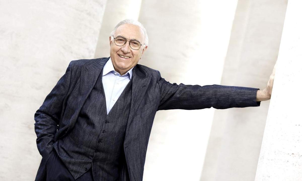 Pippo Baudo sorridente appoggiato a una colonna bianca, protagonista dello speciale Rai 1 Stasera Pippo Baudo
