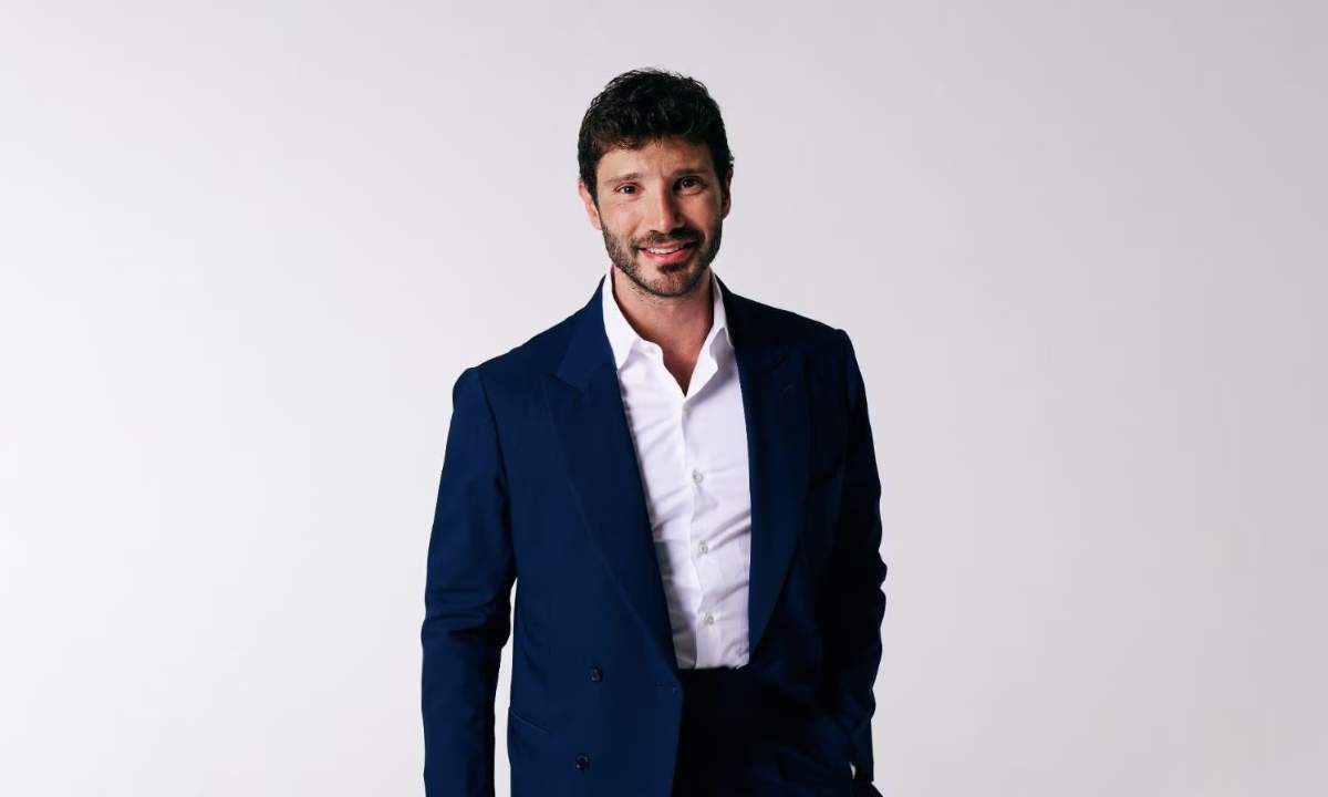 Stefano De Martino, direttore artistico di Sanremo Giovani 2026, sorride in giacca blu su sfondo neutro