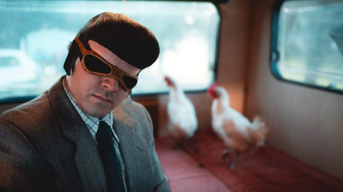 TonyPitony mascherato con occhiali da aviatore su un camper insieme a due galline