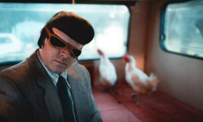 TonyPitony mascherato con occhiali da aviatore su un camper insieme a due galline