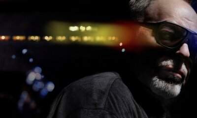Vasco Rossi di profilo con occhiali scuri, al buio, con le luci sfocate di uno stadio alle spalle