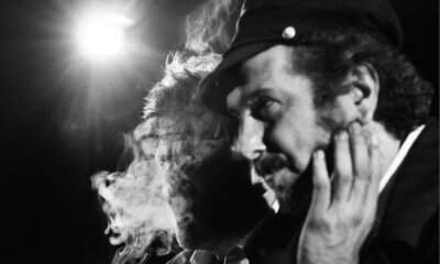 Vinicio Capossela di profilo con il cappello, in bianco e nero, tra il fumo di un palco