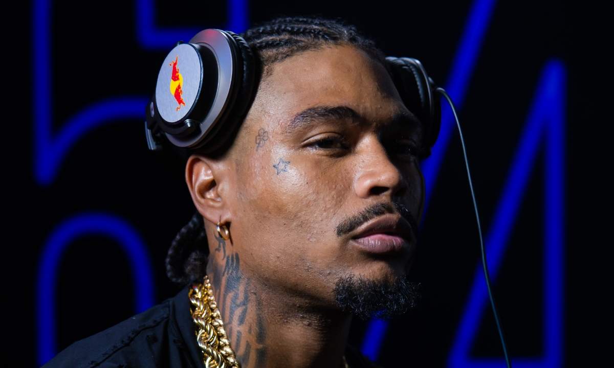 Artie 5ive con cuffie Red Bull, catena d'oro e tatuaggi sul viso, sfondo nero con neon blu