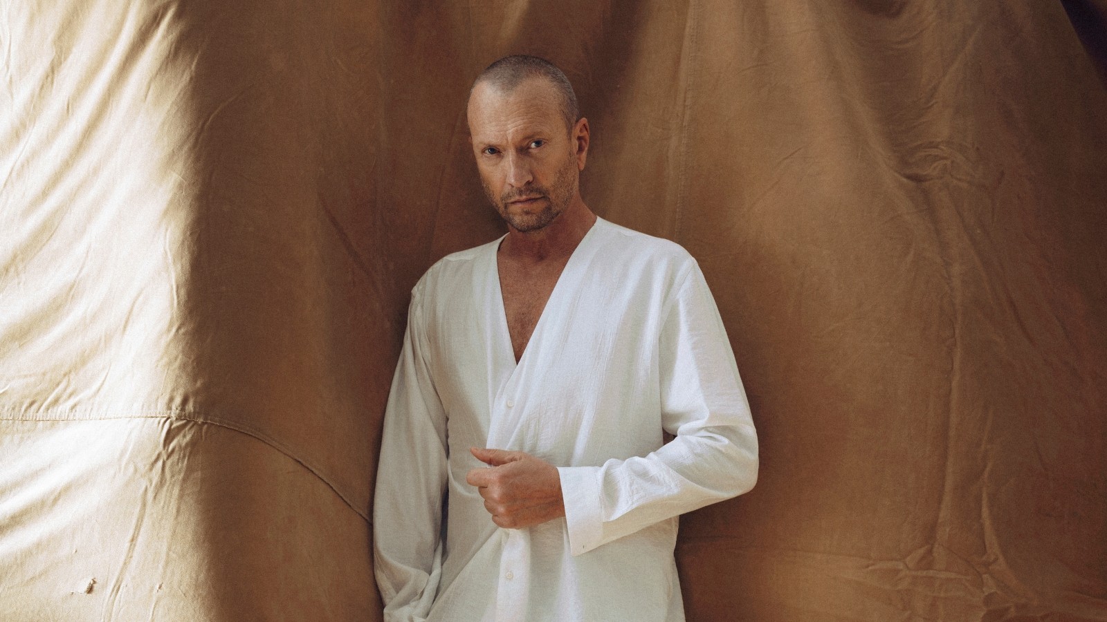 Biagio Antonacci in camicia bianca davanti a un telo color sabbia, nella foto promozionale dell'album Mustang