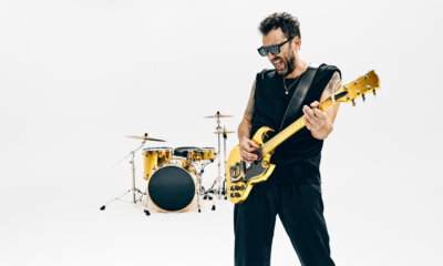 Cesare Cremonini suona una chitarra elettrica dorata davanti a una batteria dorata, su fondo bianco