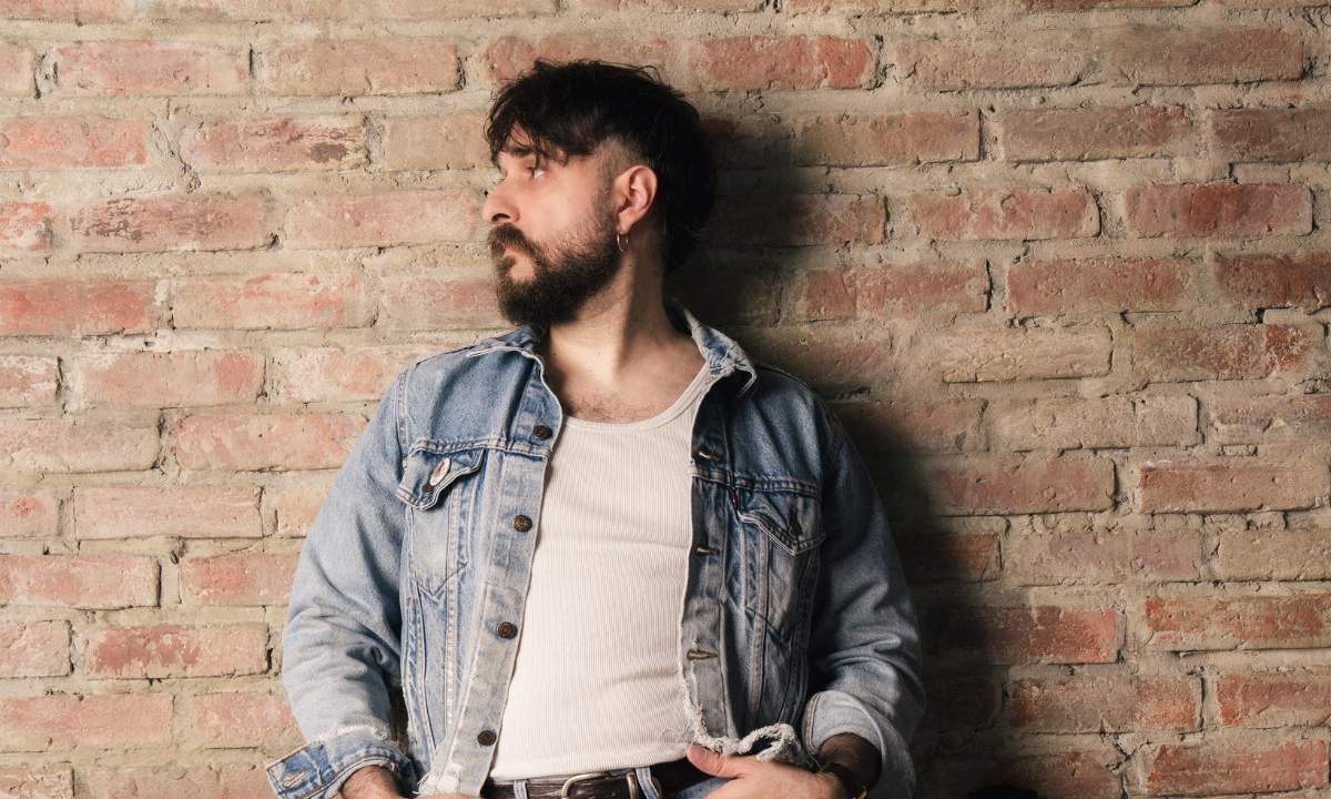 Filippo Graziani in un ritratto con giacca di jeans su un muro di mattoni