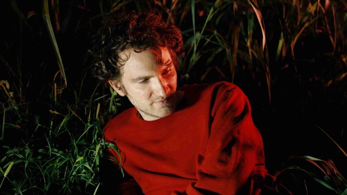 Giorgio Poi con maglione rosso seduto tra le canne, foto per il singolo Senza Colori