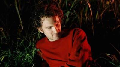 Giorgio Poi con maglione rosso seduto tra le canne, foto per il singolo Senza Colori
