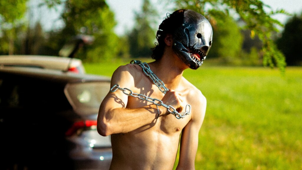 Giovane Drago con maschera e catene al collo, in una scena del video di Bruciare il mondo