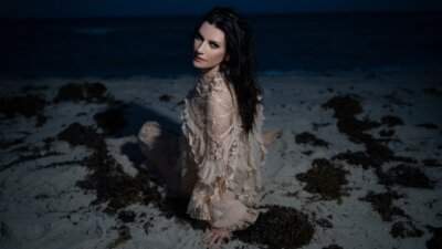 Laura Pausini seduta sulla sabbia di una spiaggia di notte, con un abito di pizzo color cipria e i capelli scuri sciolti