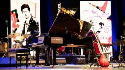 Il palco del Premio Tenco 2025 con il pianoforte a coda e il ritratto di Luigi Tenco sullo sfondo