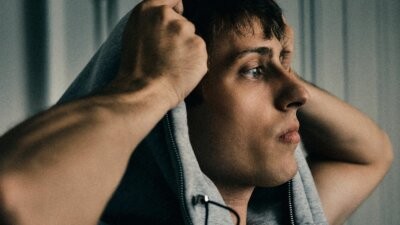 sangiovanni nella foto promozionale dell'album TUTTO BENE GRAZIE, di profilo con le mani sul cappuccio della felpa grigia