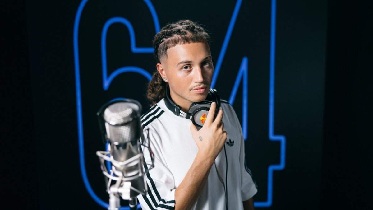 Sayf con le cuffie al collo davanti a un microfono e alla scritta 64 al neon blu