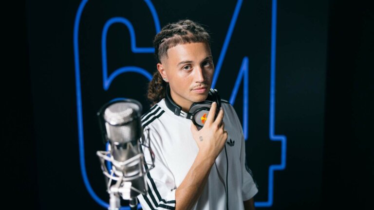 Sayf con le cuffie al collo davanti a un microfono e alla scritta 64 al neon blu