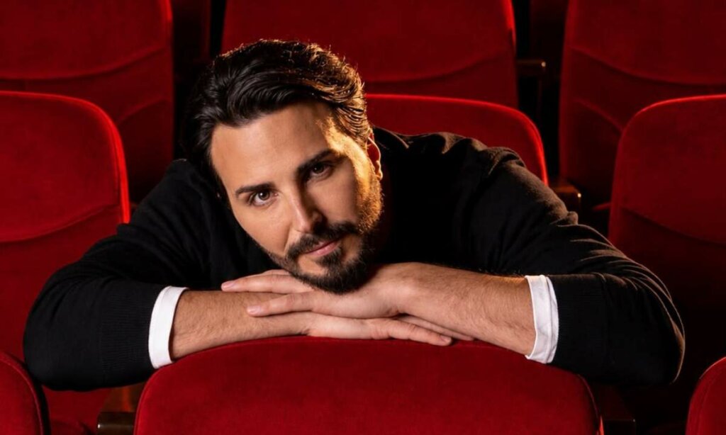 Tony Colombo appoggiato a una poltrona rossa di teatro