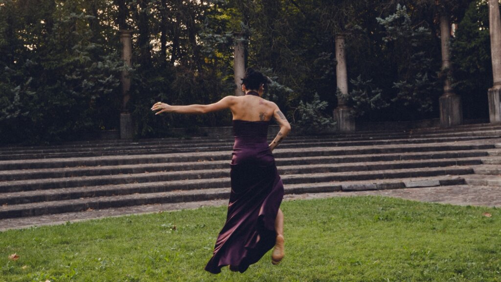 Angelina Mango di spalle, in movimento e con un abito viola scuro, in un parco davanti a una gradinata, nell'immagine che annuncia il singolo Vita da adulti