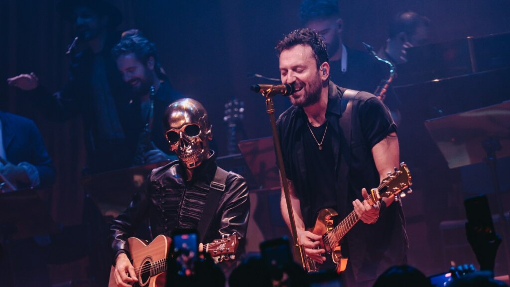 SIG, il personaggio dal teschio dorato, suona la chitarra acustica accanto a Cesare Cremonini sul palco di Londra