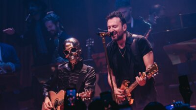 SIG, il personaggio dal teschio dorato, suona la chitarra acustica accanto a Cesare Cremonini sul palco di Londra