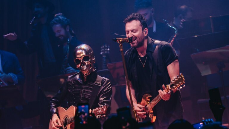 SIG, il personaggio dal teschio dorato, suona la chitarra acustica accanto a Cesare Cremonini sul palco di Londra