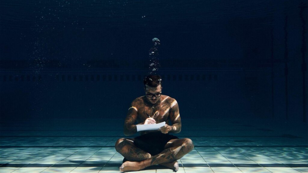 Geolier seduto sul fondo di una piscina mentre scrive su un foglio