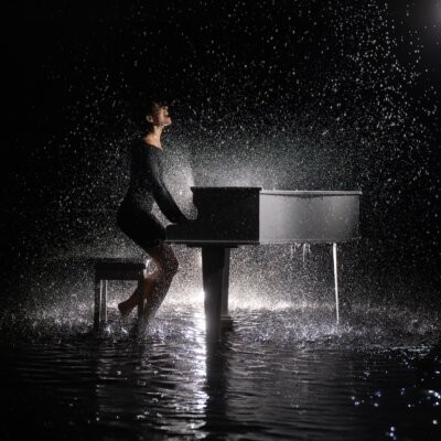 Copertina del singolo Piccole cose di Giordana Angi, con una persona al pianoforte a coda sotto la pioggia
