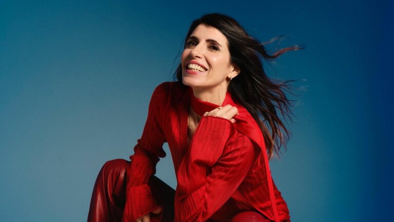 Giorgia sorride con un maglione rosso su sfondo blu