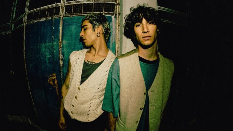 Dodo e Jeanvier, il duo livornese JED entrato ad Amici 26, in gilet davanti a una porta di ferro verde