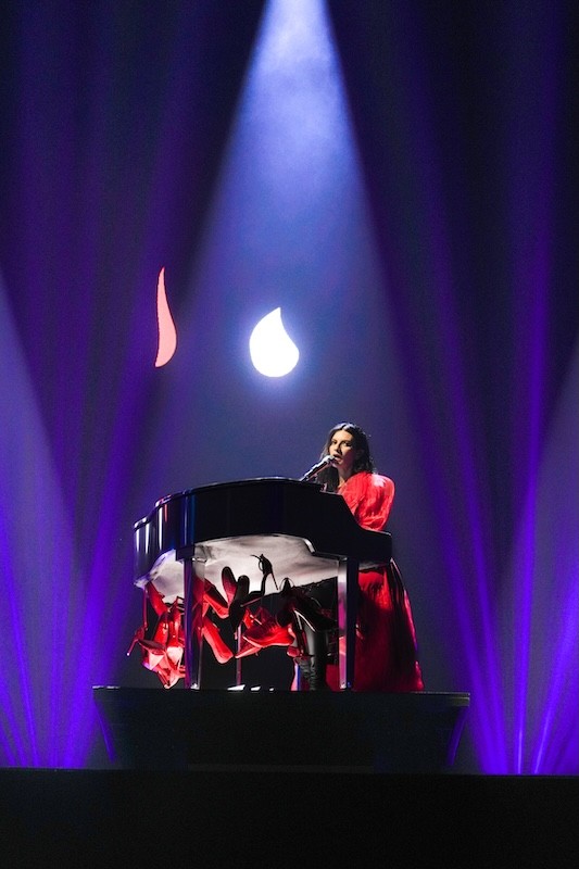 Laura Pausini in abito rosso al pianoforte, tra fasci di luce viola, al PalaUnical di Mantova