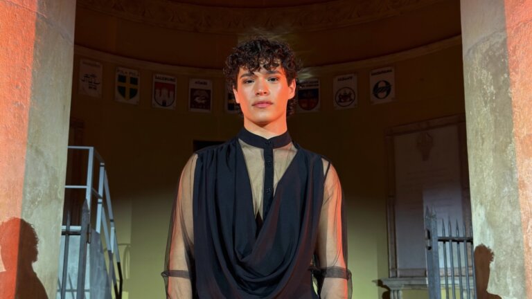 Manuel Meledina, il cantante genovese entrato ad Amici 26, con una camicia nera trasparente sotto un portico illuminato